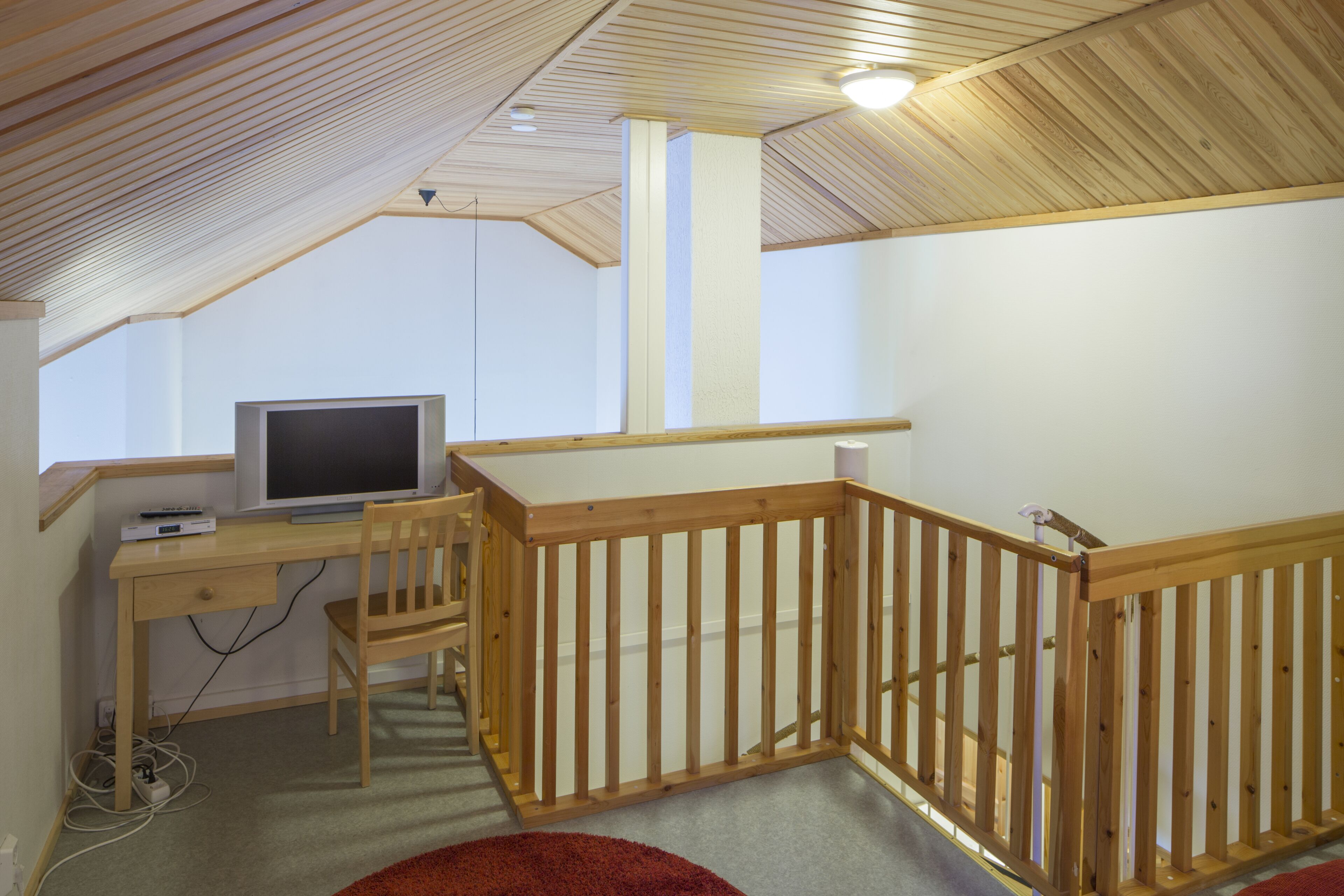 A room with a wooden desk, a chair, a television, and a wooden railing.