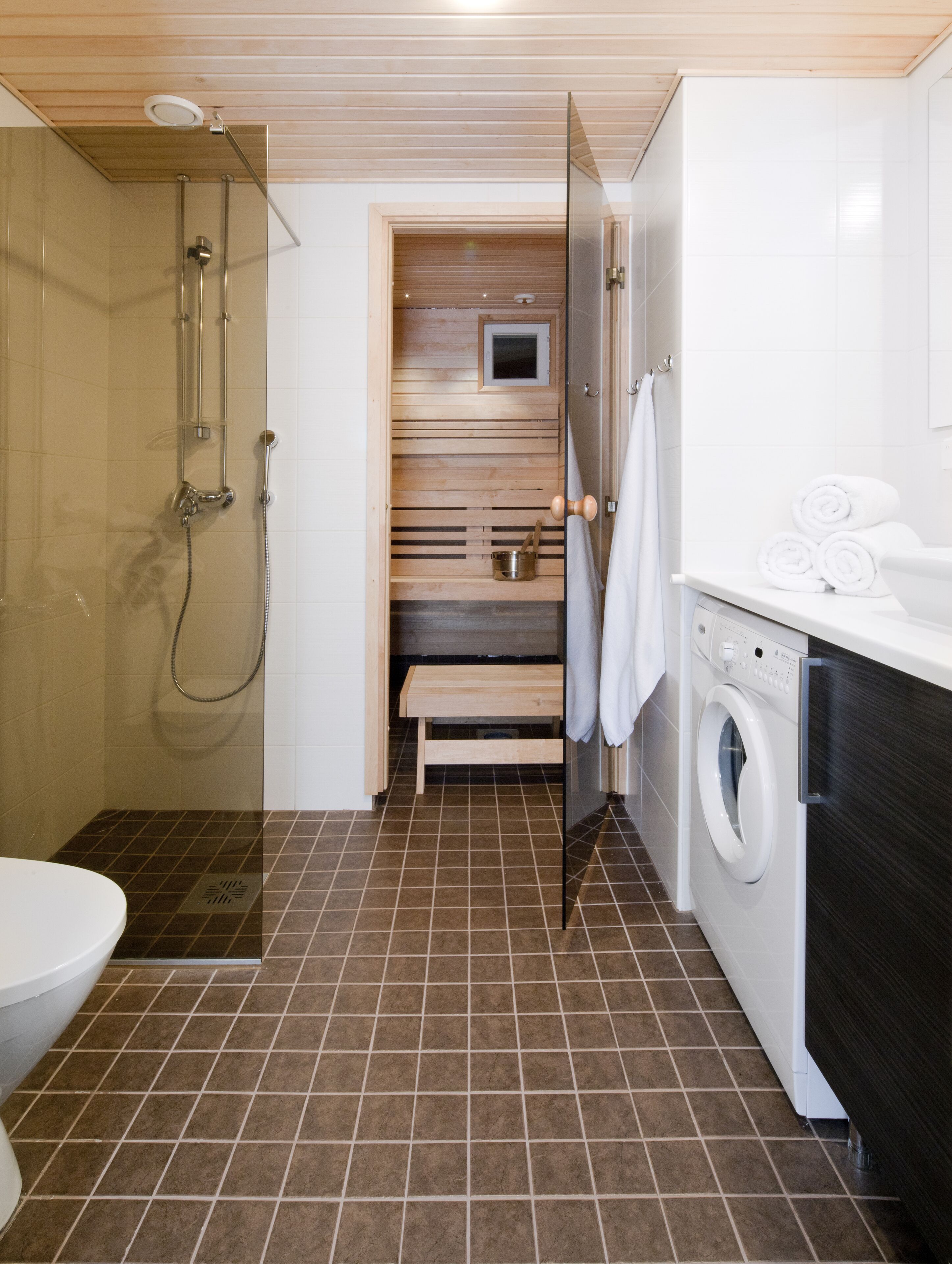 Un baño pequeño con ducha, inodoro y lavadora.