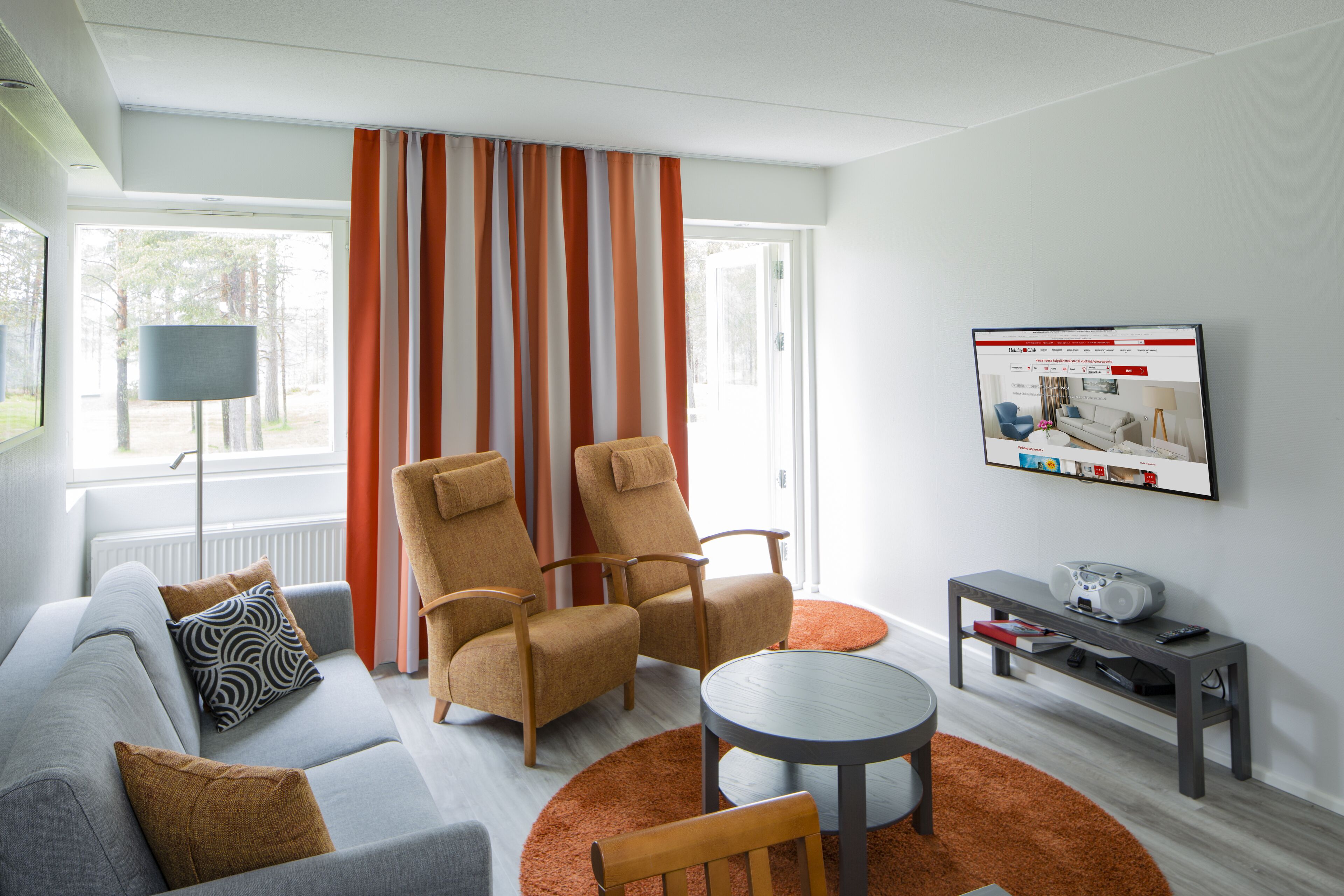 Una sala de estar moderna con un sofá gris, dos sillones, una mesita de centro y un televisor montado en la pared.