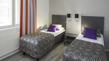 Une chambre d’hôtel avec deux lits simples, une petite table, une table de chevet, une fenêtre avec des rideaux et un haut-parleur fixé au mur.