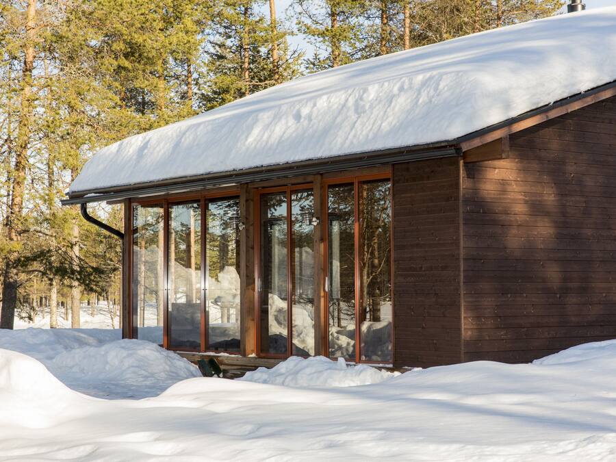 Una cabaña de madera con ventanas amplias y techo cubierto de nieve, rodeada de árboles.