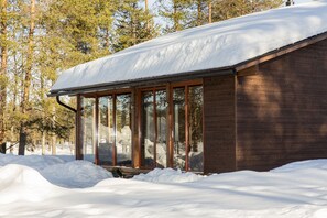 A wooden cabin with large windows and a snow-covered roof, surrounded by trees. - Holiday Club Kuusamo Tropiikki Apartments (Kuusamo)