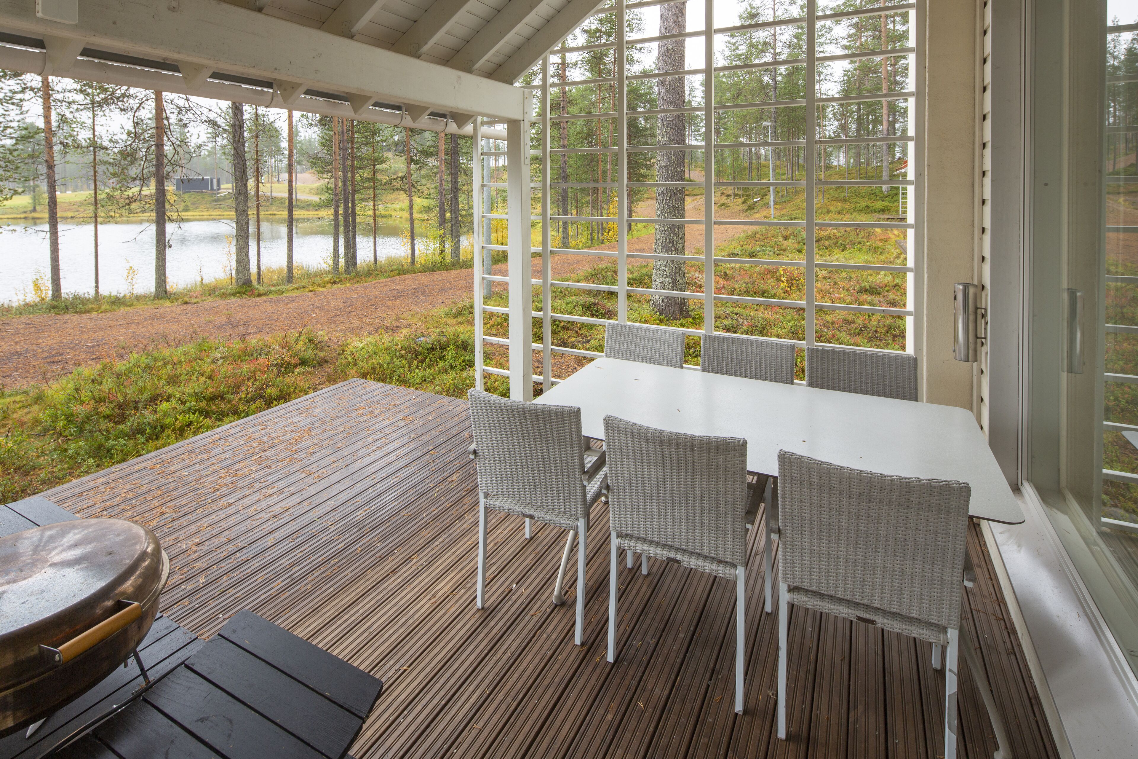 Een overdekt terras met een tafel en stoelen, met uitzicht op een waterpartij en een bebost gebied.