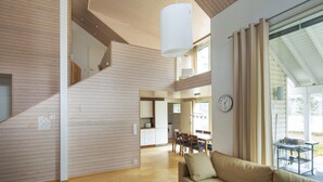 A modern interior with a wooden floor, a dining area with chairs and a table, a sofa, and a hanging light fixture.
