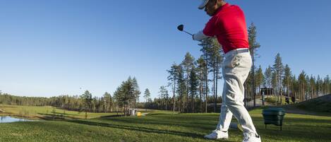 A golf course with a player in a red shirt and white pants preparing to swing.