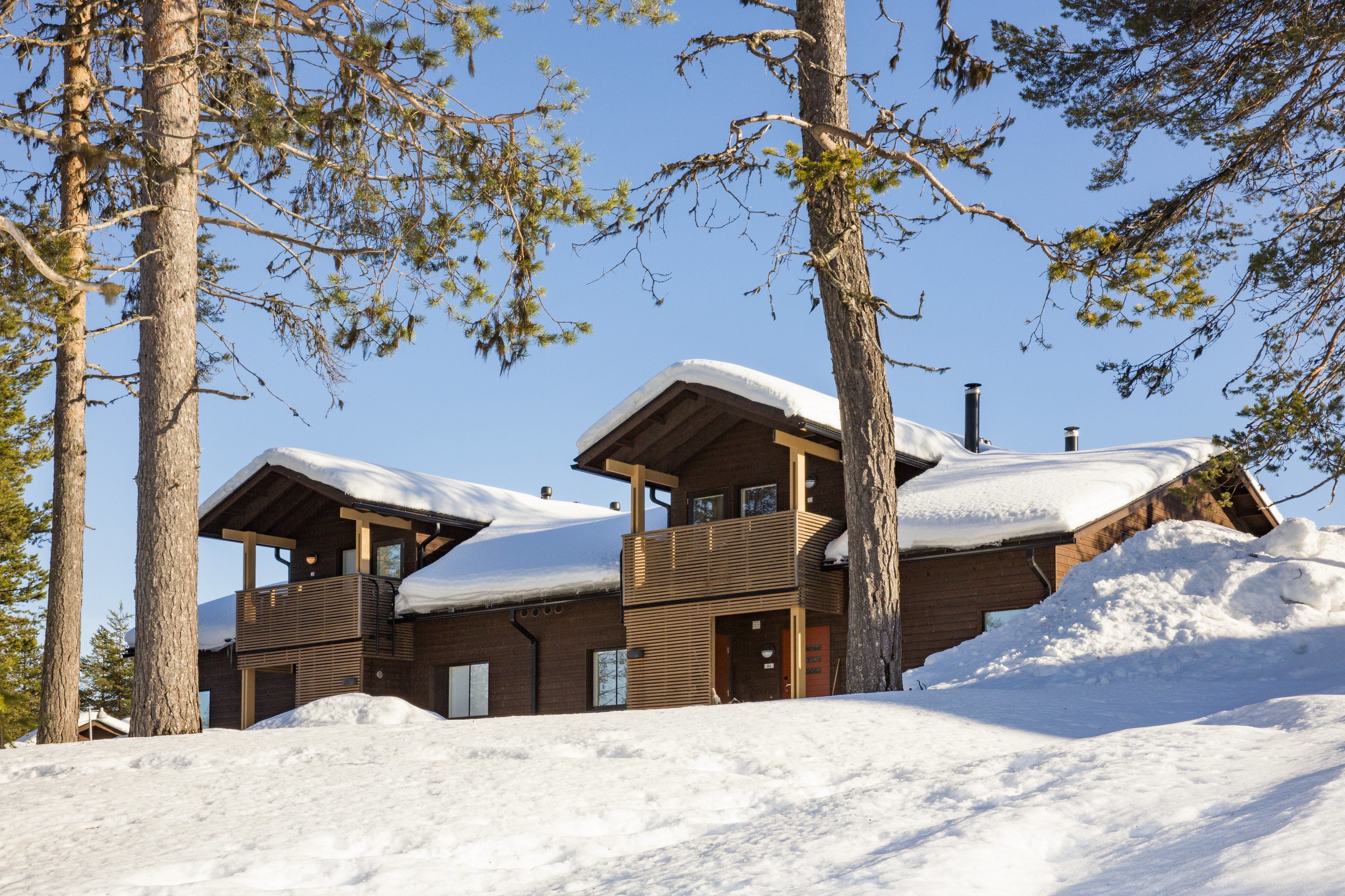 A wooden cabin with a balcony, surrounded by trees and covered in snow.