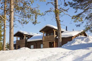 A wooden cabin with a balcony, surrounded by trees and covered in snow. - Holiday Club Kuusamo Tropiikki Apartments (Kuusamo)