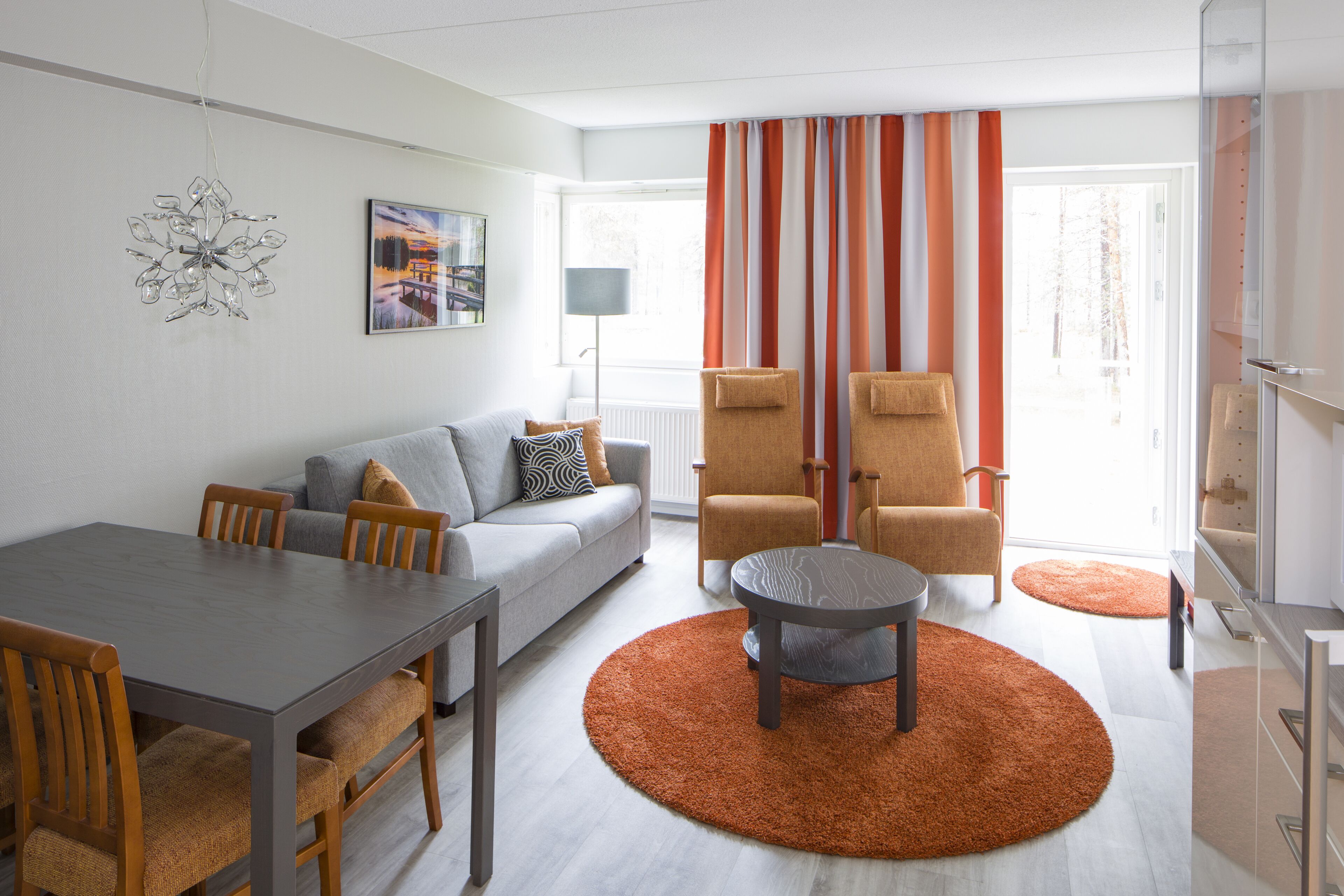 A modern living room with a grey sofa, wooden chairs, a dining table, and a round coffee table.