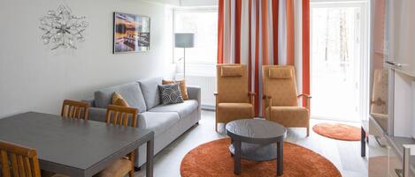 A modern living room with a grey sofa, wooden chairs, a dining table, and a round coffee table.