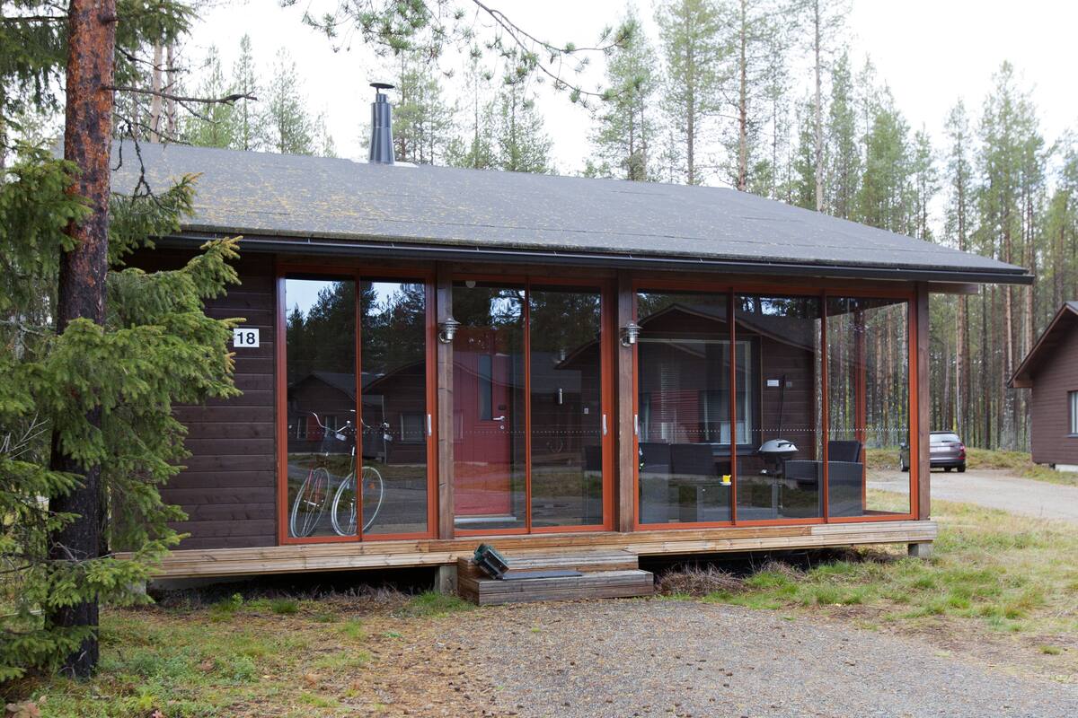 Eine Holzhütte mit großen Glasfenstern, einer Holzterrasse und einem Schild mit der Nummer 18.