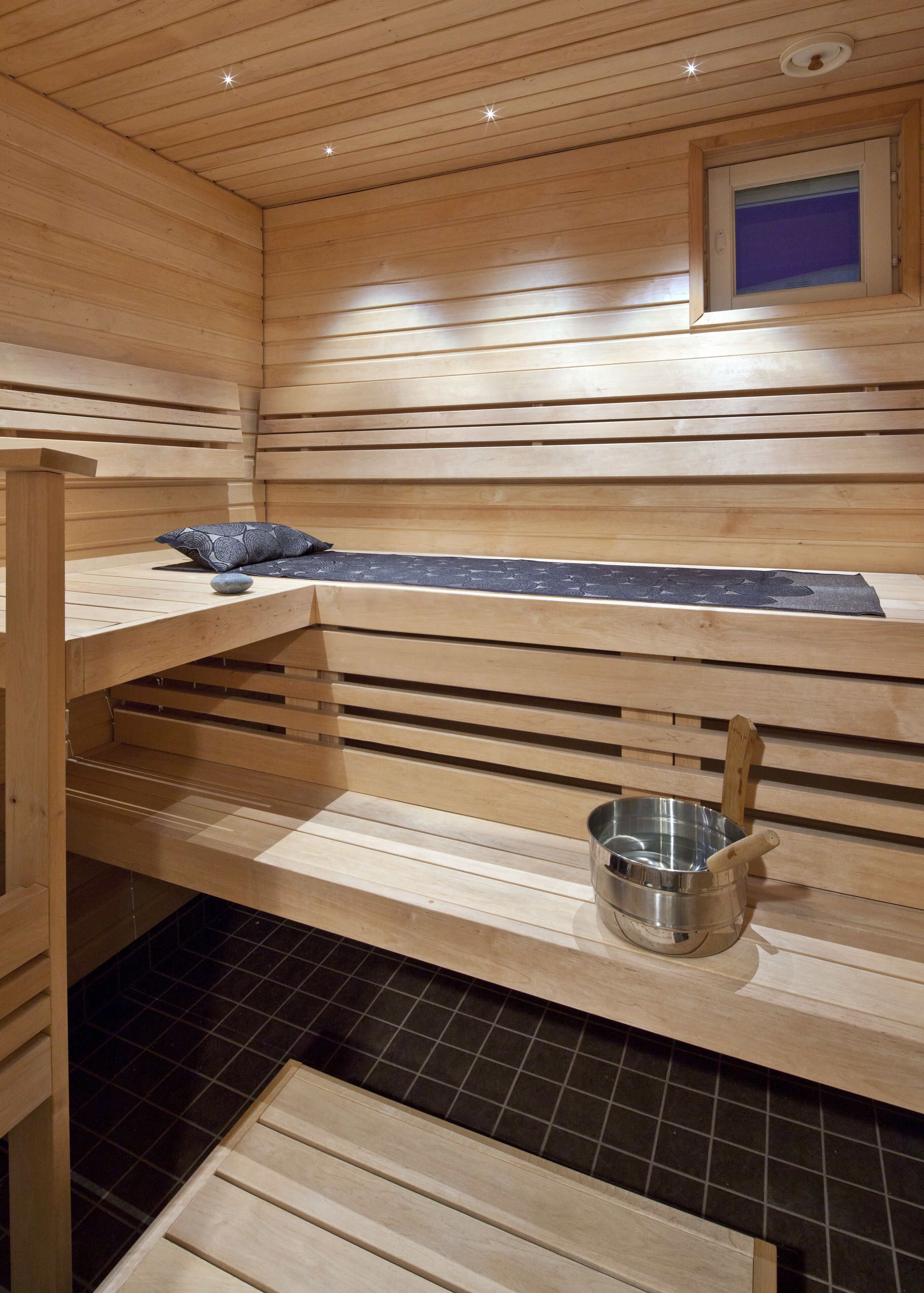 A sauna with wooden benches, a metal bucket, and a small window.
