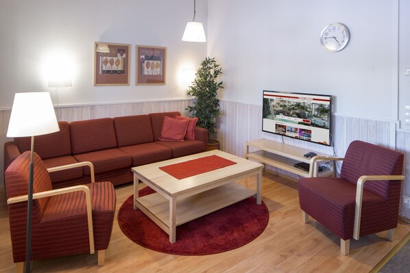 A modern living room with a sofa, armchairs, a coffee table, a TV, and a plant.