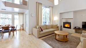 A spacious living room with a sofa, coffee table, and dining area with chairs. There is a fireplace and a television.