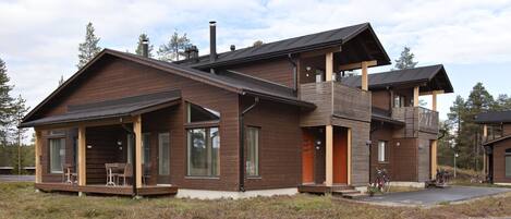 A modern two-story cabin with a balcony, large windows, and a covered porch area.