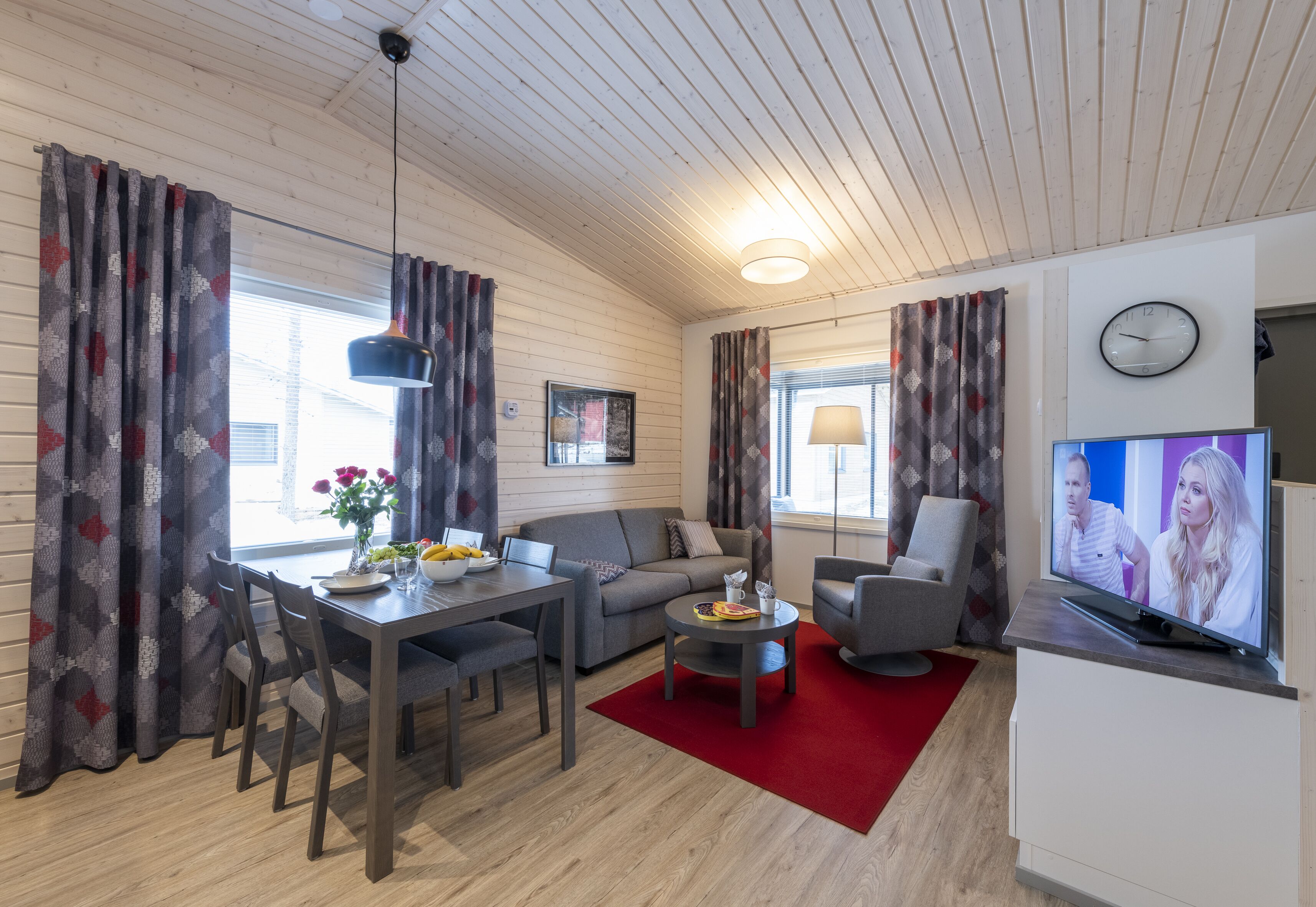 Ein modernes Wohnzimmer mit Essbereich, einer Couch, einem Fernseher und einem roten Teppich.