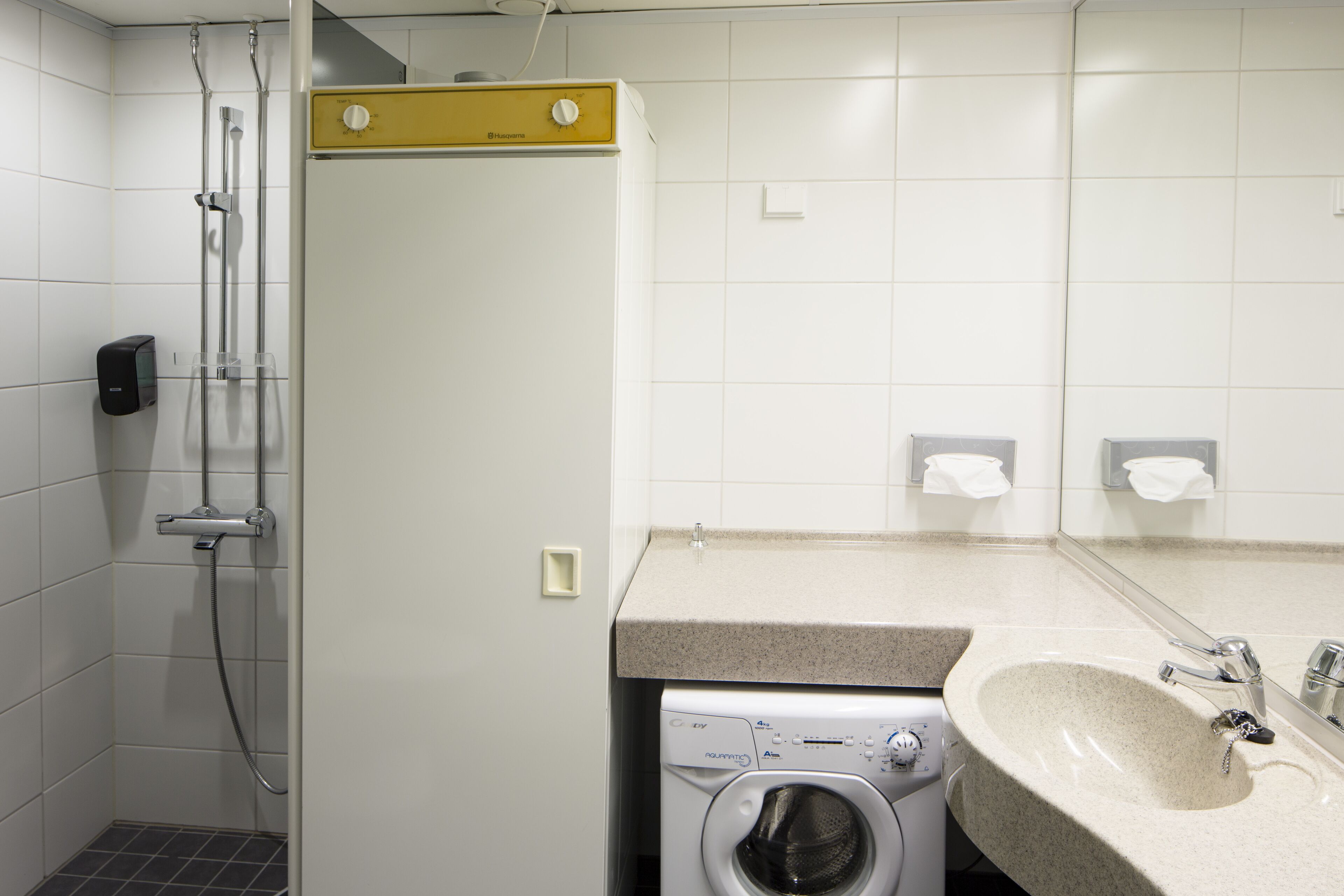 A compact hotel bathroom with a washing machine, a sink, and a shower.
