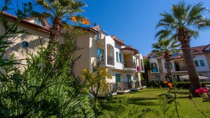 A multi-story building with balconies, surrounded by lush greenery and palm trees. - Rebin Beach Hotel (Fethiye)