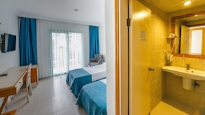 A hotel room with a desk, two beds, a chair, and a bathroom with a sink and mirror. - Rebin Beach Hotel (Fethiye)