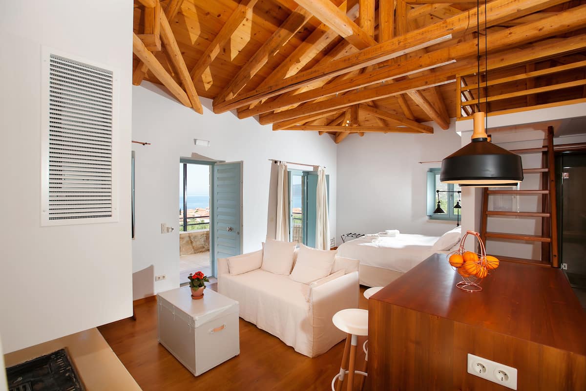 A modern, open-plan living space with a wooden ceiling, a white sofa, a small white cabinet, and a wooden table with a basket of oranges.