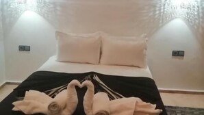 A bed with two pillows, a black and white striped blanket, and two towels folded into swans. There are three wall-mounted hats with text. - Riad Dar Nakhla (Marrakech)