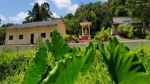 A building with a yellow facade, a small pavilion with a Buddha statue, and lush greenery in the foreground. - Hotel Alas Garden (Trincomalee)
