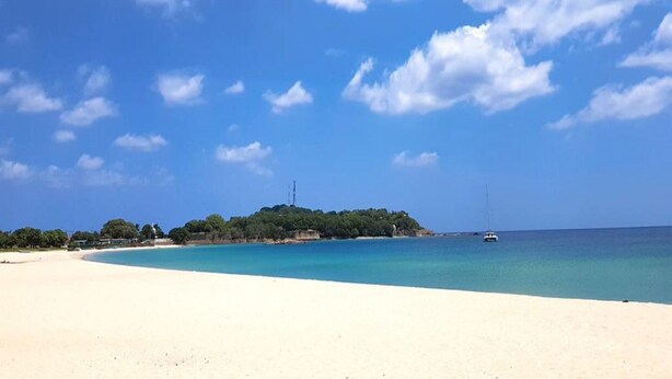 A beach with clear blue water, a sandy shore, and a small island with trees in the distance. - Hotel Alas Garden (Trincomalee)