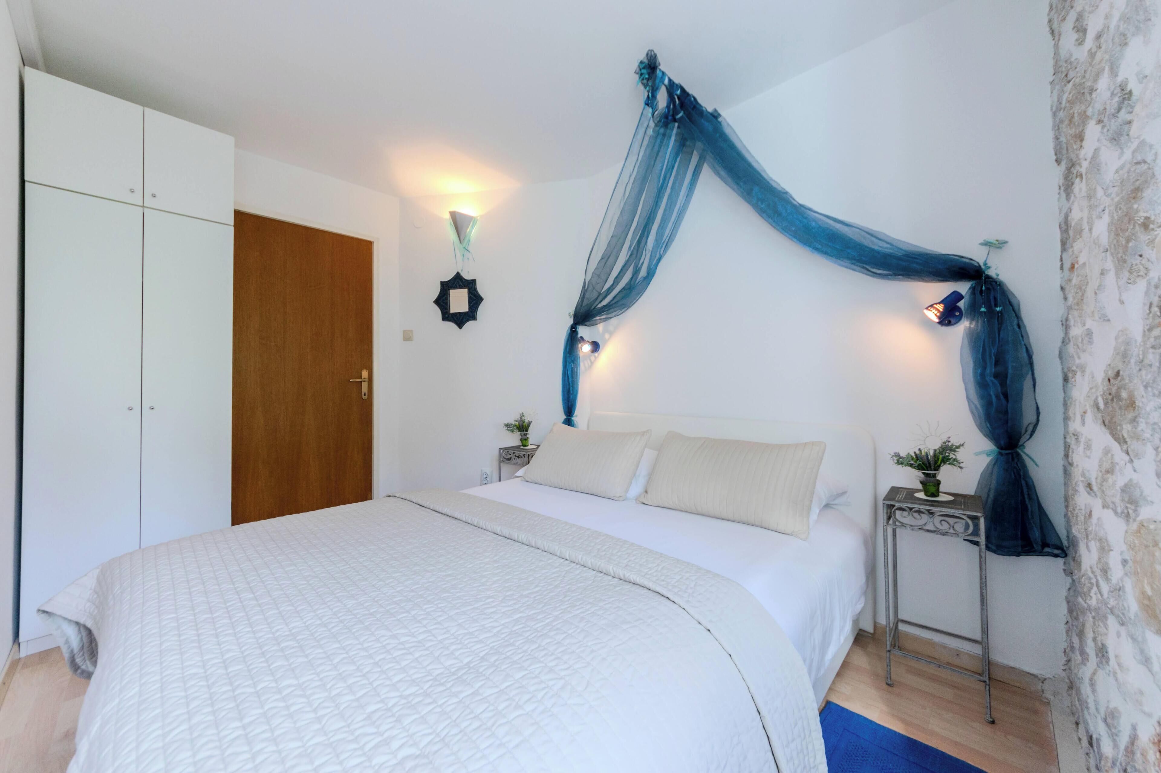 A bedroom with a bed, a wardrobe, a nightstand with a lamp, and a wall-mounted light fixture.