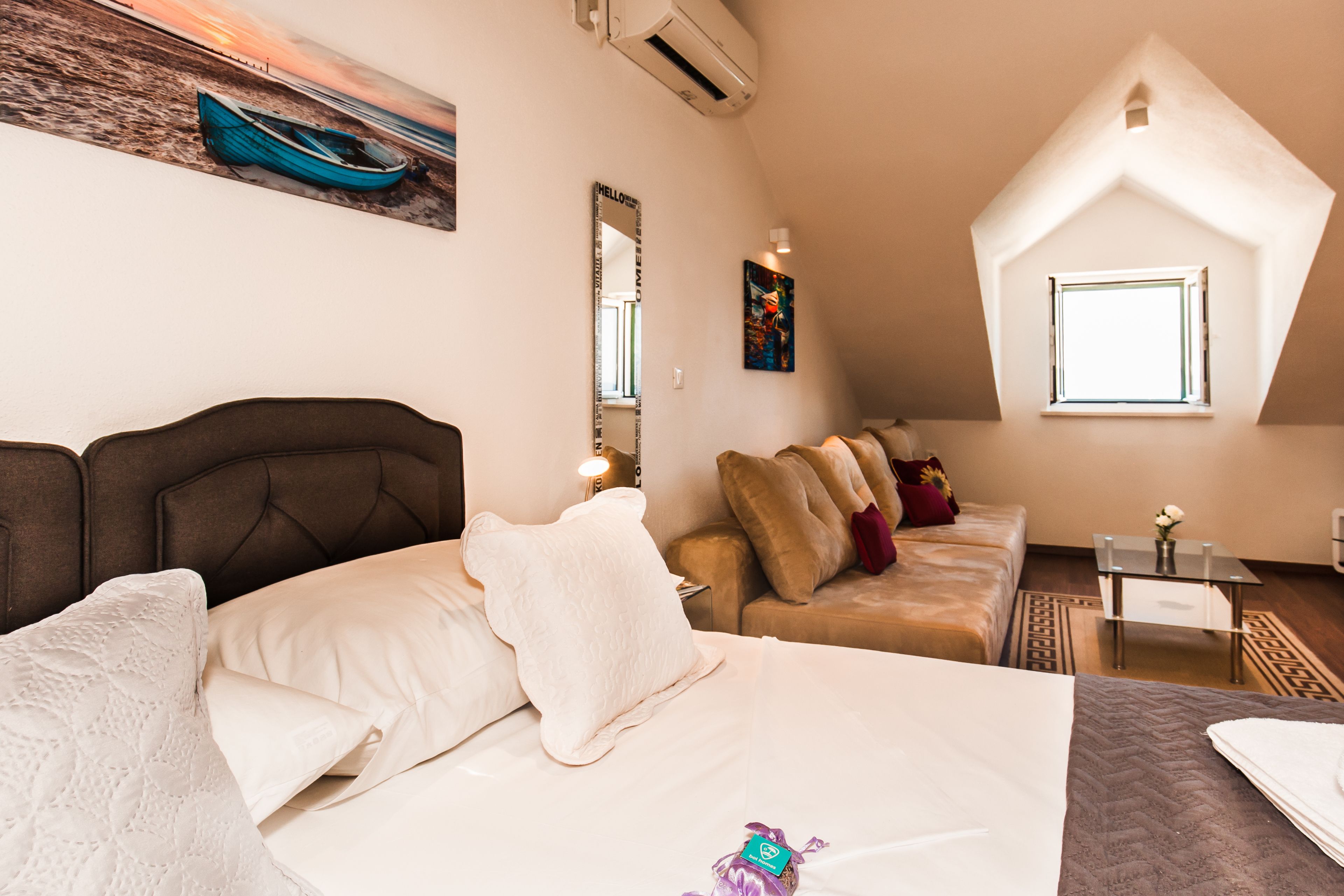 A bedroom with a bed, a sofa, a small table, a mirror, and a window.