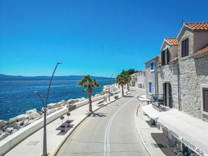 Une rue côtière bordée de bâtiments en pierre, une mer d’un bleu limpide et une route sinueuse.