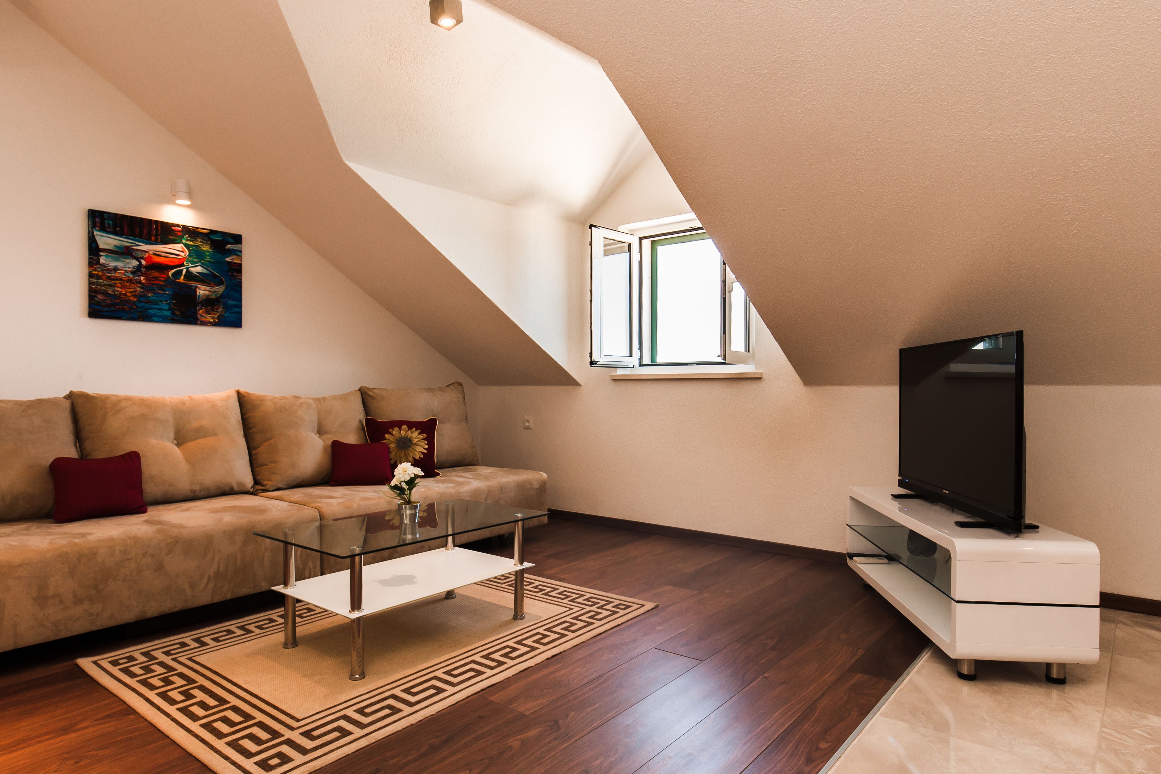 A modern living room with a sloped ceiling, a sofa, a coffee table, a TV on a stand, and a window.