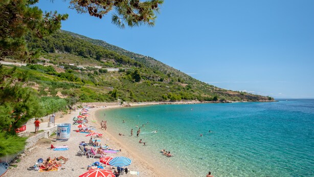 A beach with clear turquoise water, people sunbathing and swimming, and umbrellas providing shade. - Luxury Seaside Apartments (Bol)
