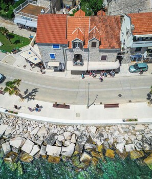 Vista aérea de los Apartamentos Riva Mare, con edificios de piedra, una calle pavimentada y un litoral rocoso.