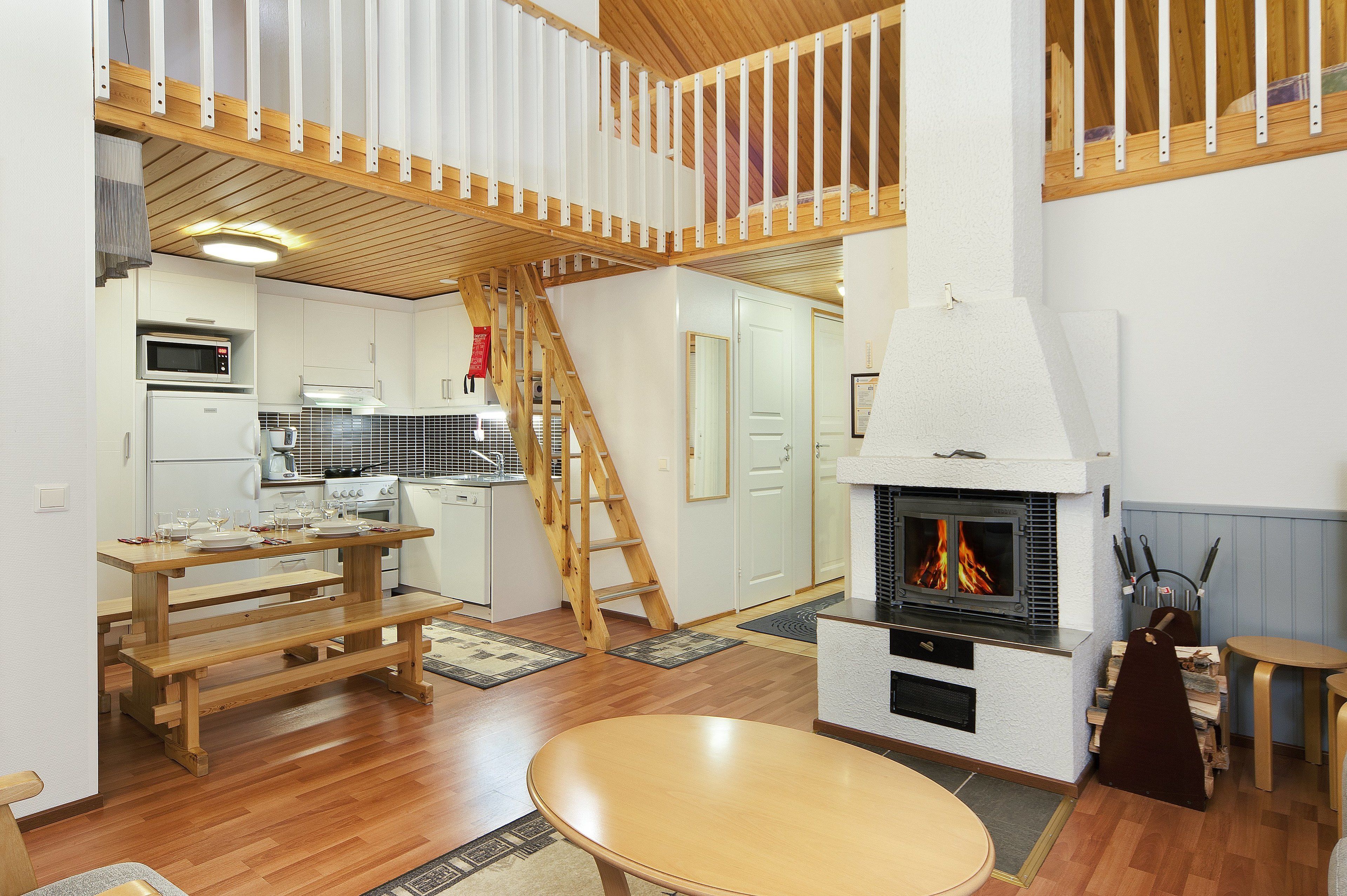 A modern kitchen with wooden flooring, a built-in microwave, and a stove. There is a wooden bench and a round table in the living area.