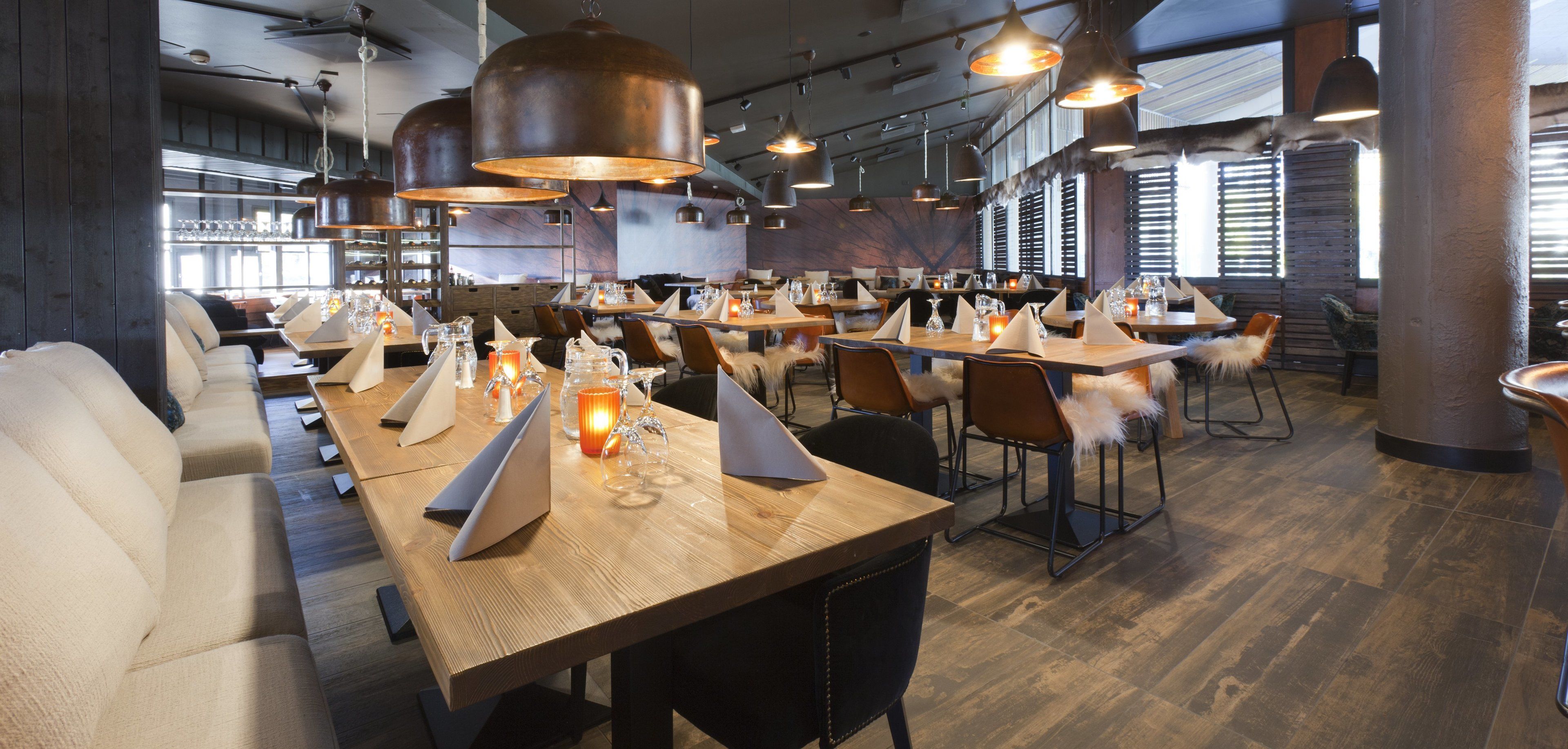 A modern restaurant with wooden tables, leather seating, and pendant lighting.