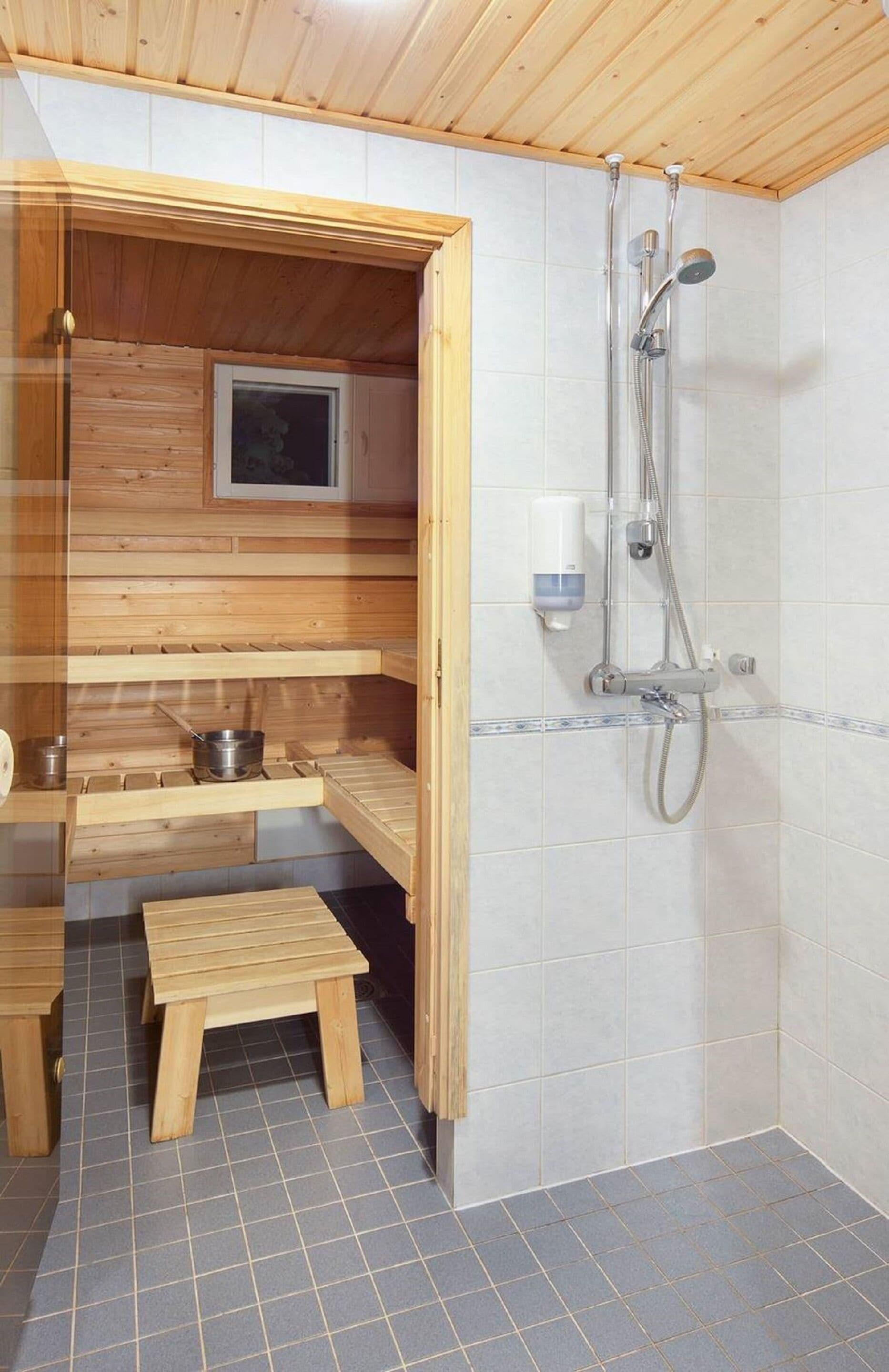 A sauna room with wooden benches, a small table, and a shower area with tiled walls and a wooden ceiling.