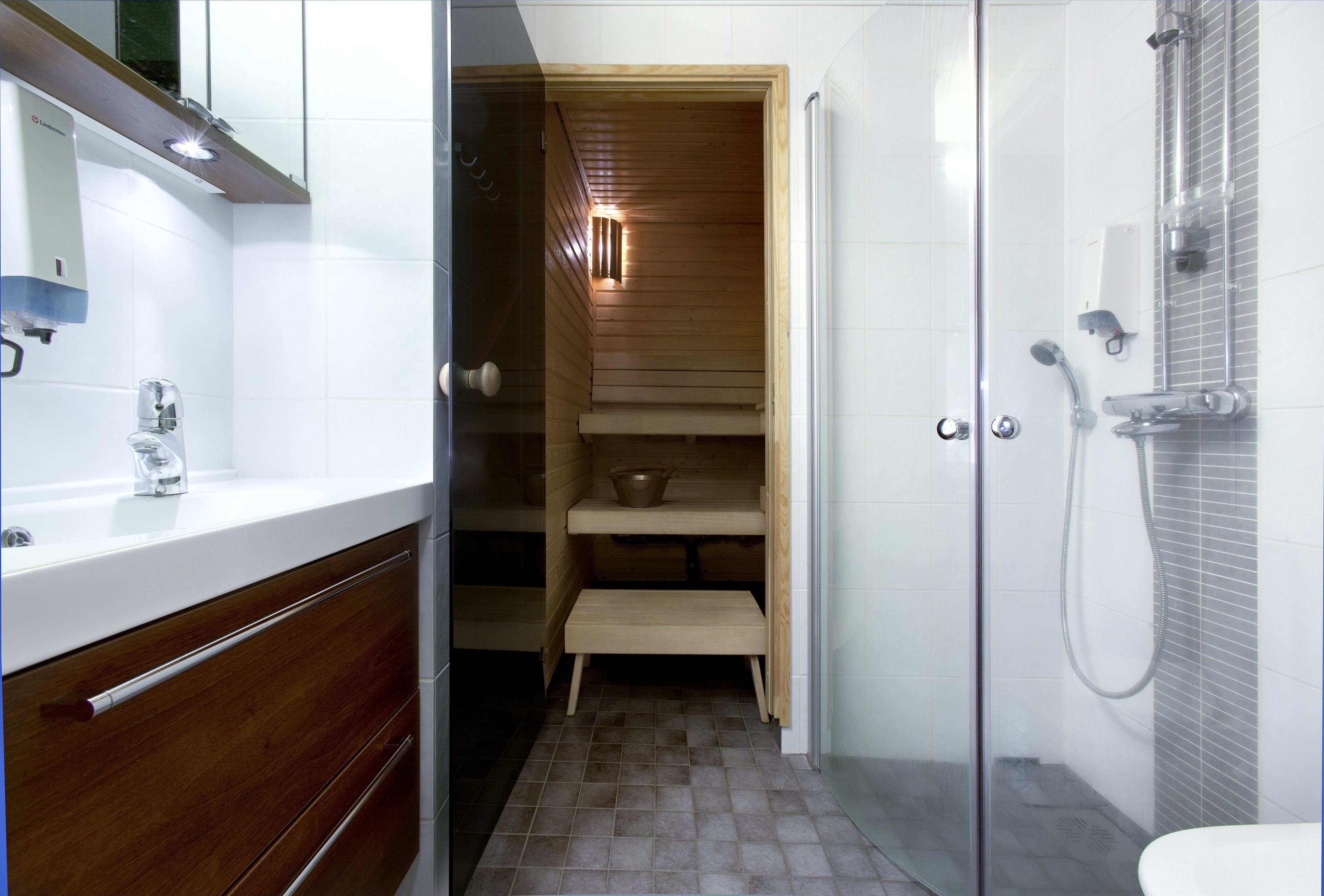Un baño moderno con cabina de ducha de vidrio, sauna de madera y lavamanos blanco con espejo.