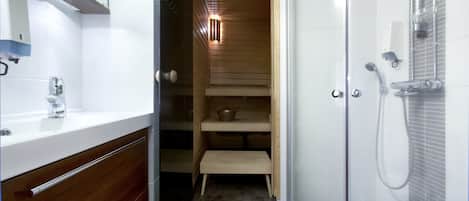 Un baño moderno con cabina de ducha de vidrio, sauna de madera y lavamanos blanco con espejo.