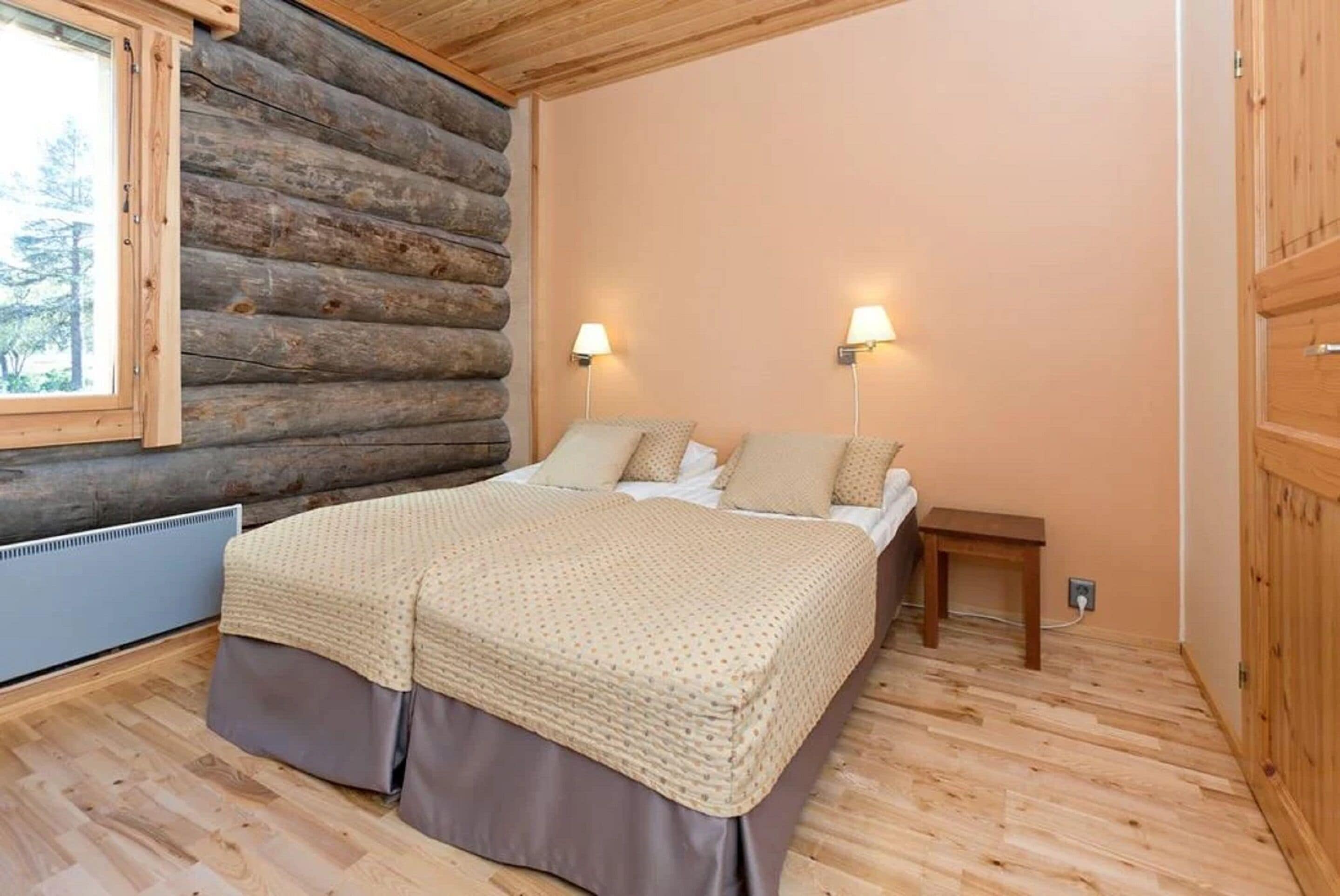Ein Schlafzimmer in einer Blockhütte mit einem Bett, zwei Nachttischlampen und einem Fenster.