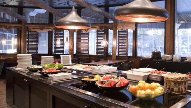 Disposição de buffet com diversos alimentos e área de estar com mesas e cadeiras.