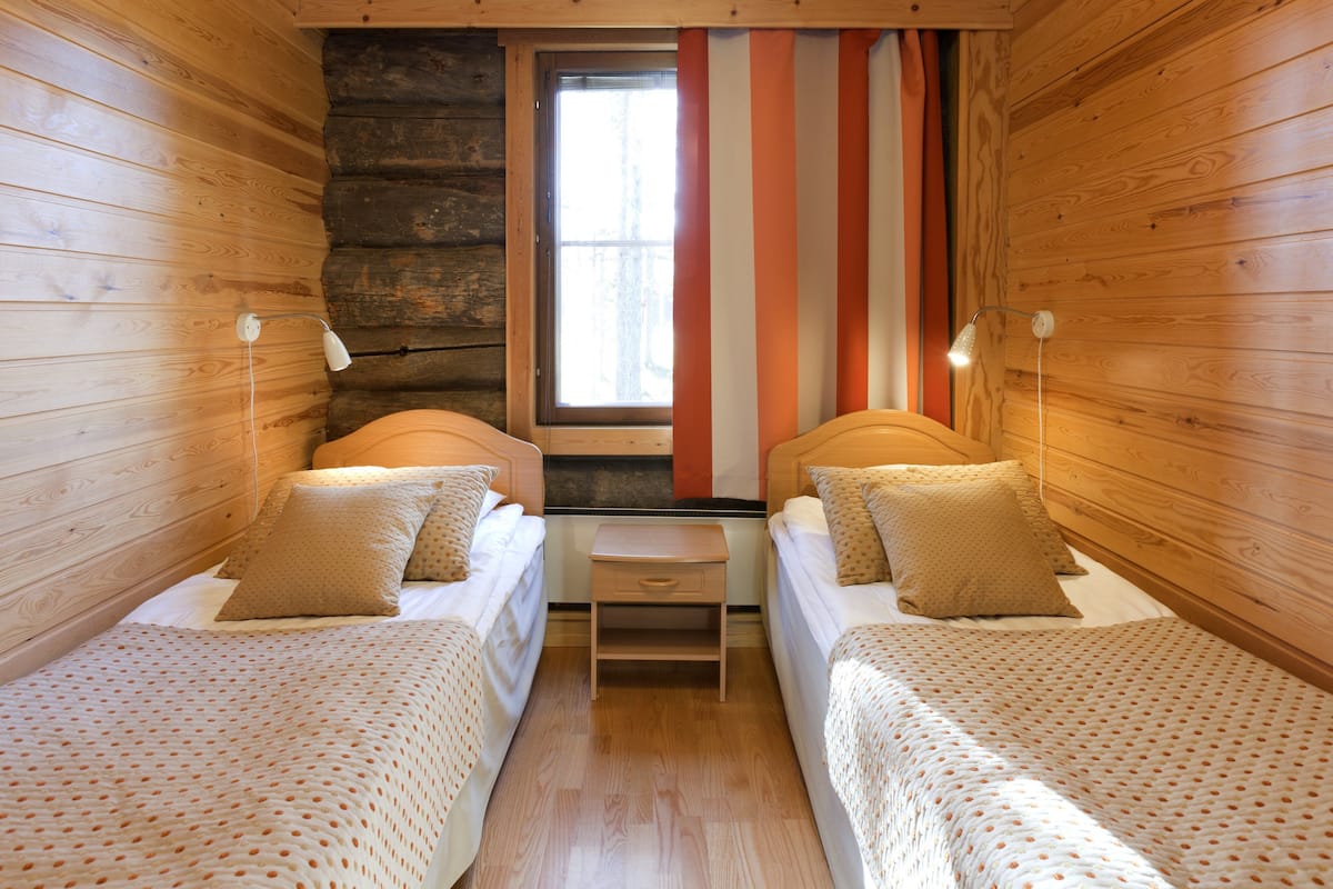 A cabin-style room with two single beds, a small table, and a window with curtains.