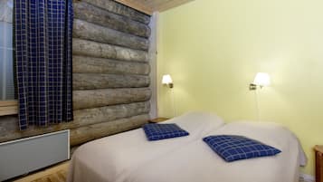 A room with a log wall, two bedside tables with lamps, a bed with two pillows, and a window with curtains.