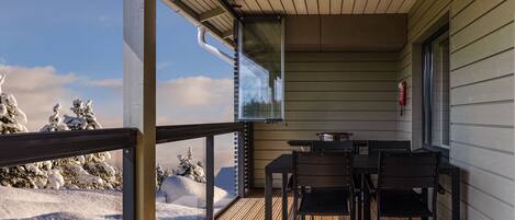 Una terraza de madera con una mesa y sillas, con vistas a un paisaje nevado.