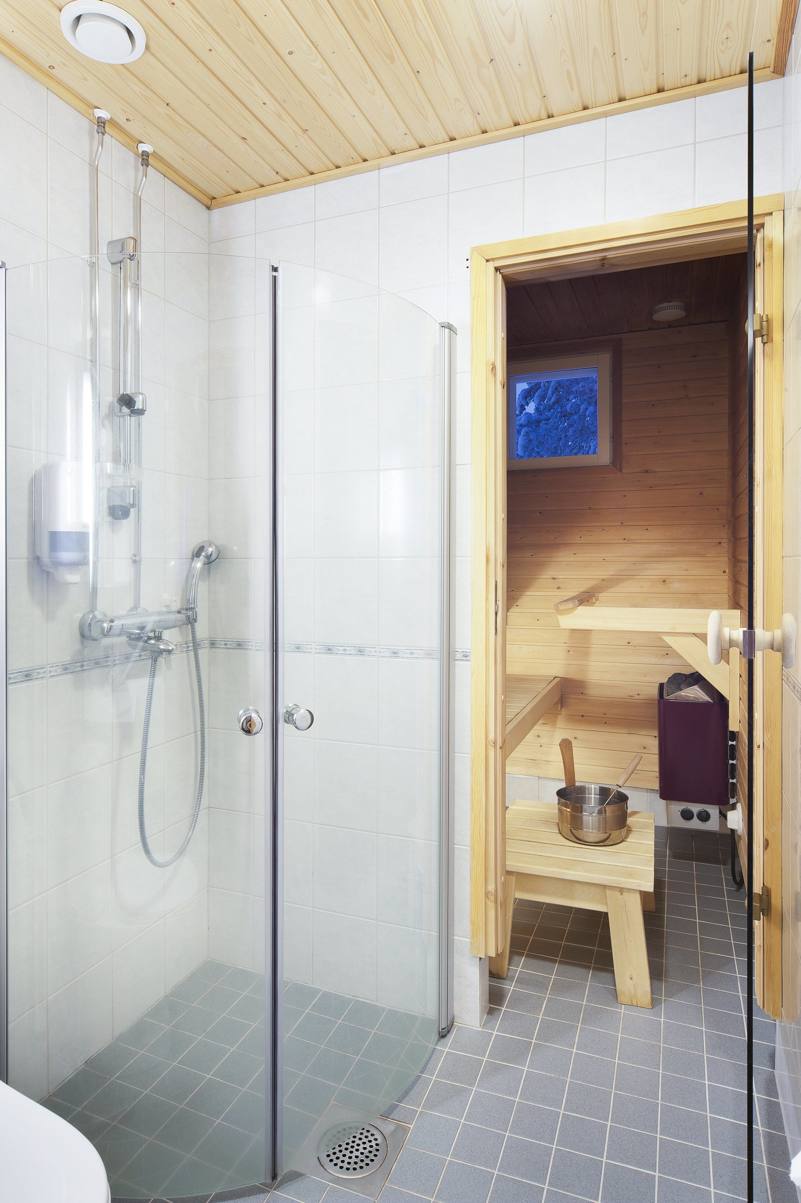 Een moderne badkamer met een douchecabine van glas, witte betegelde wanden en een houten sauna.