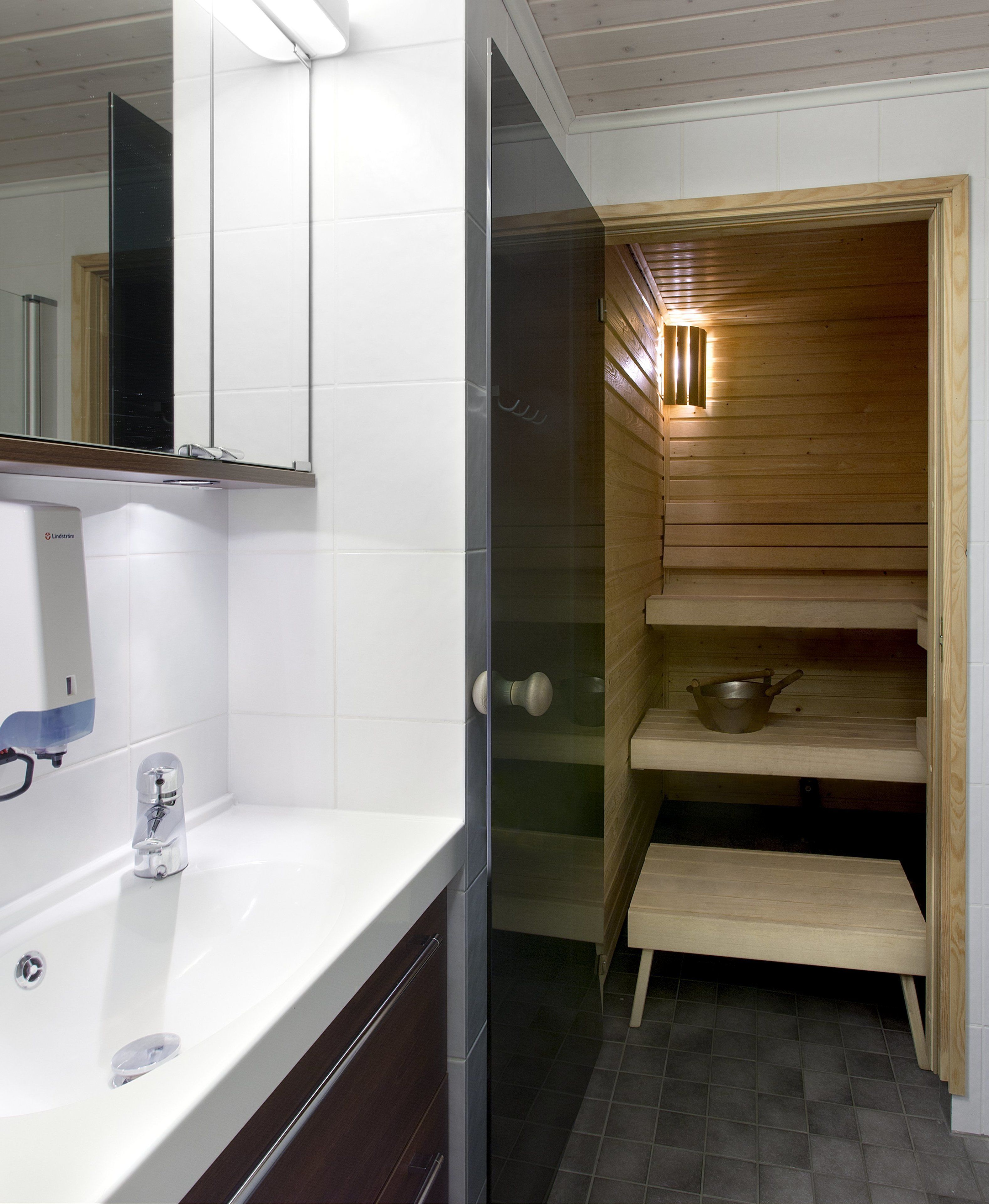 Un baño con lavamanos blanco, un espejo y una cabina de ducha con escalones de madera.