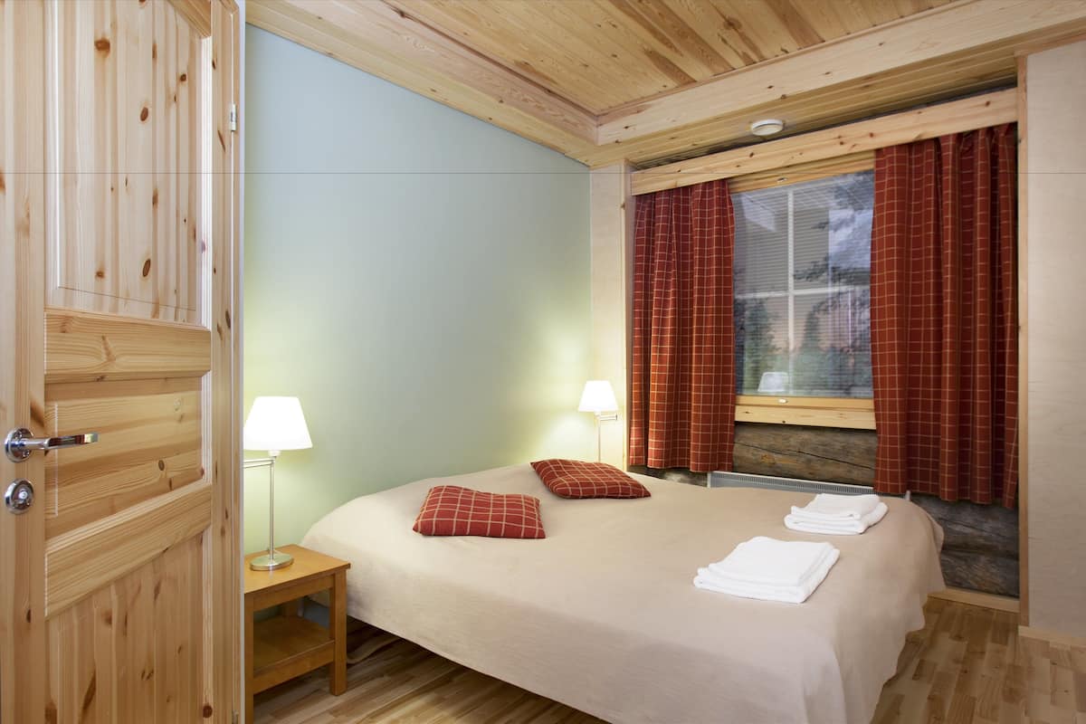 A room with a bed, two bedside lamps, a window with curtains, and a wooden wardrobe.