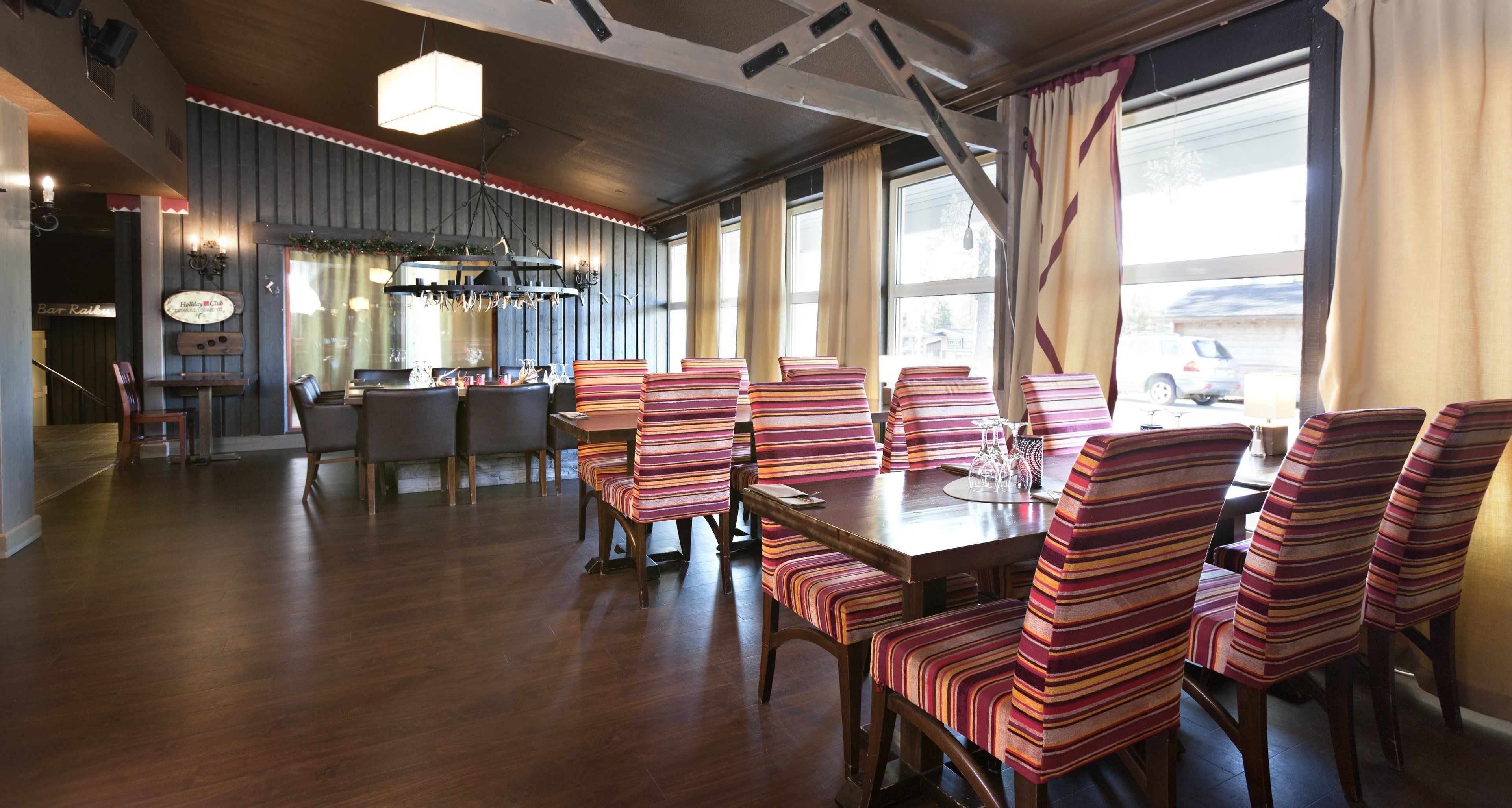 Un espace repas avec des chaises à rayures et une table en bois, de grandes fenêtres et un bar à l’arrière-plan.