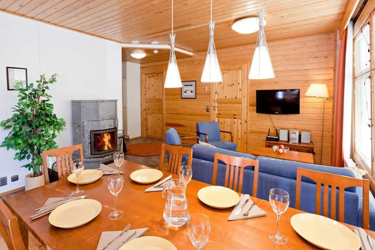 A cozy room with a wooden interior, a fireplace, a dining table set for four, and a comfortable seating area with a sofa and chairs.
