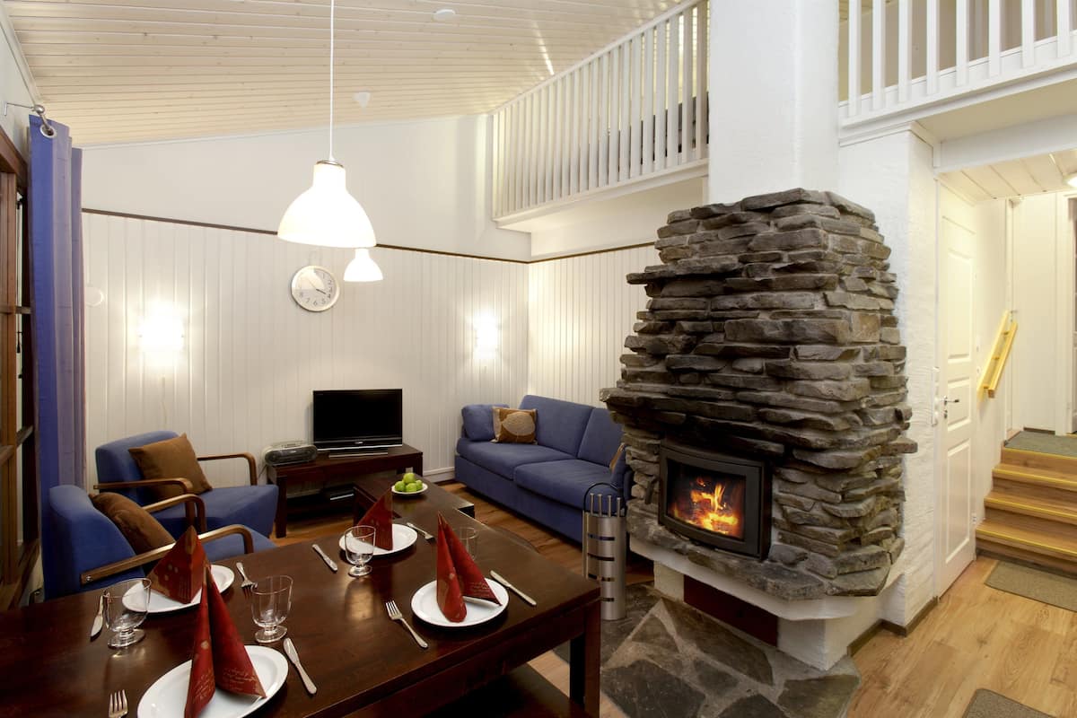 A modern living room with a stone fireplace, a dining area with set tables, a blue sofa, and a television.
