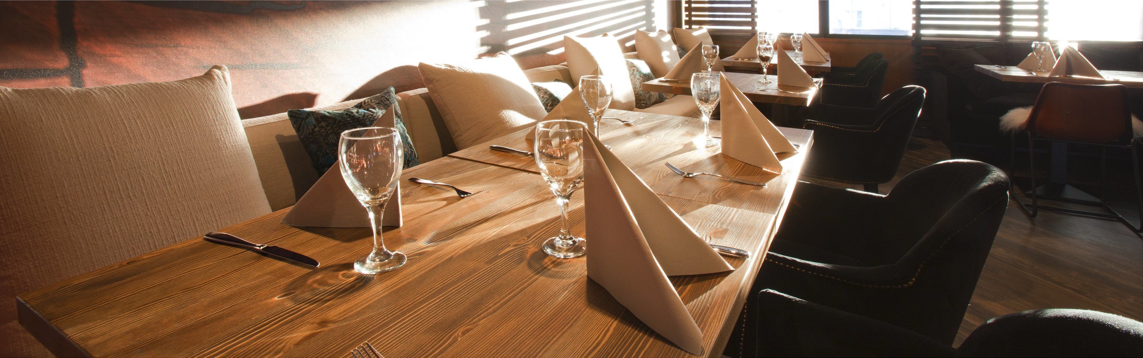 A dining area with wooden tables, chairs, and wine glasses set for a meal.