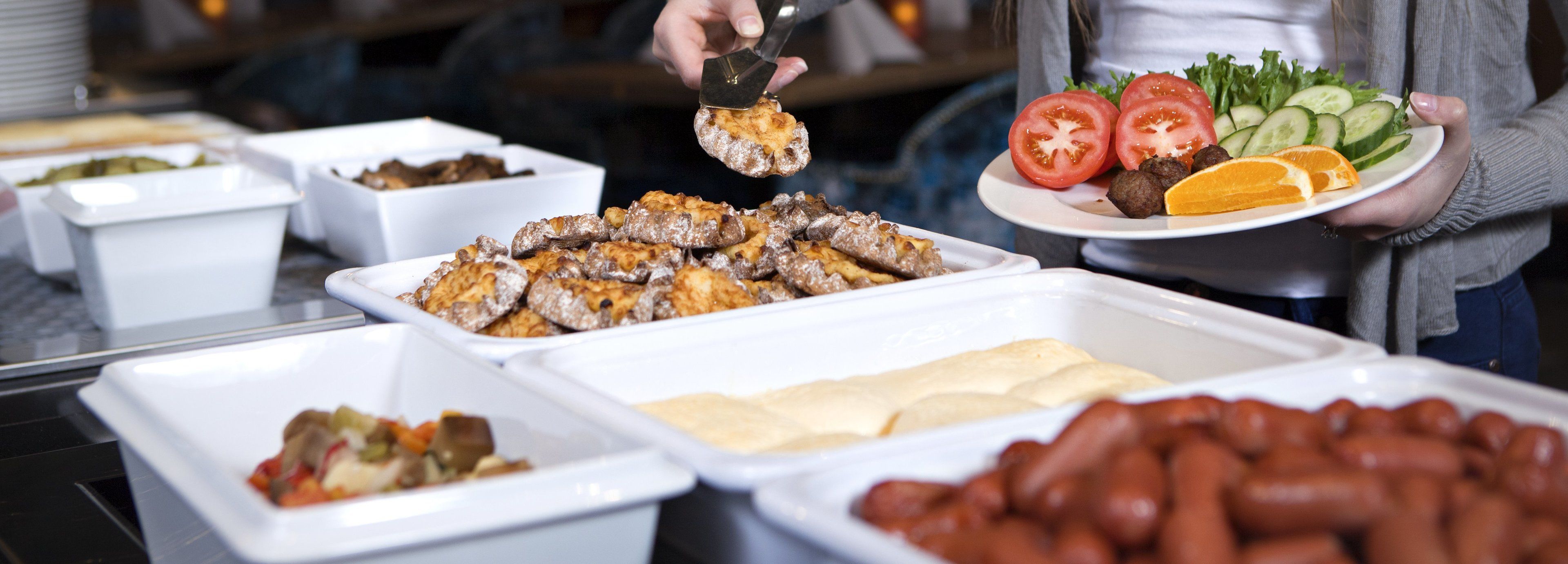 Ein reichhaltiges Buffet mit verschiedenen Speisen, darunter Fleisch, Gemüse und ein Teller mit Tomaten, Gurken und Fleischbällchen.